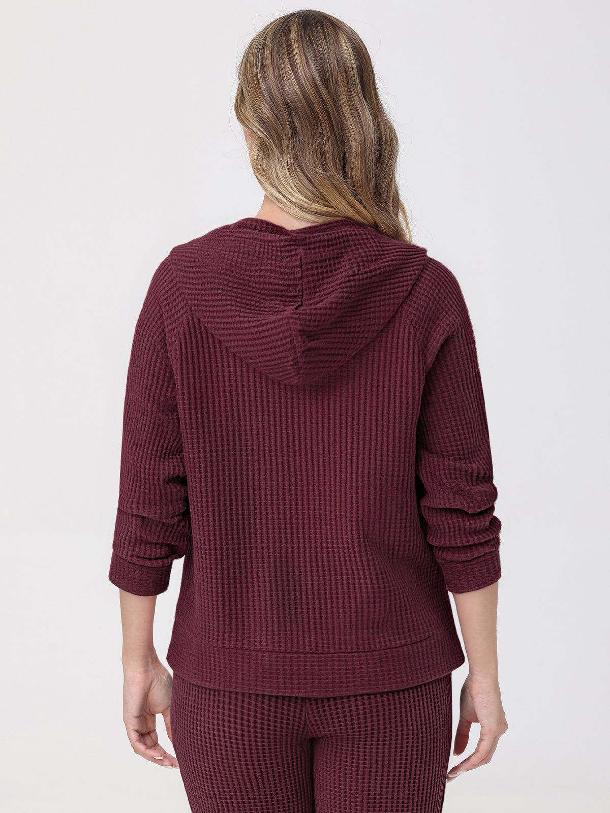Person wearing a burgundy waffle knit hoodie and pants on a light gray background