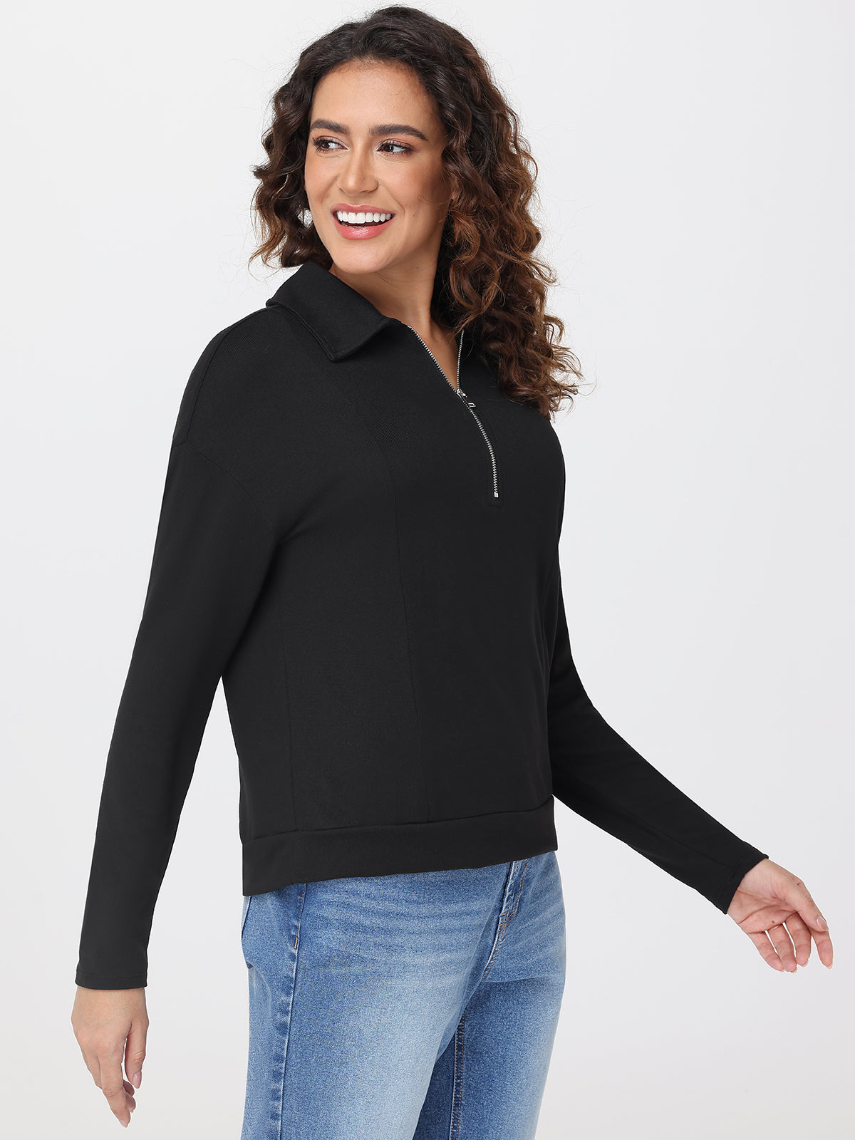 Woman wearing a black long-sleeve top with a collar and blue jeans on a white background