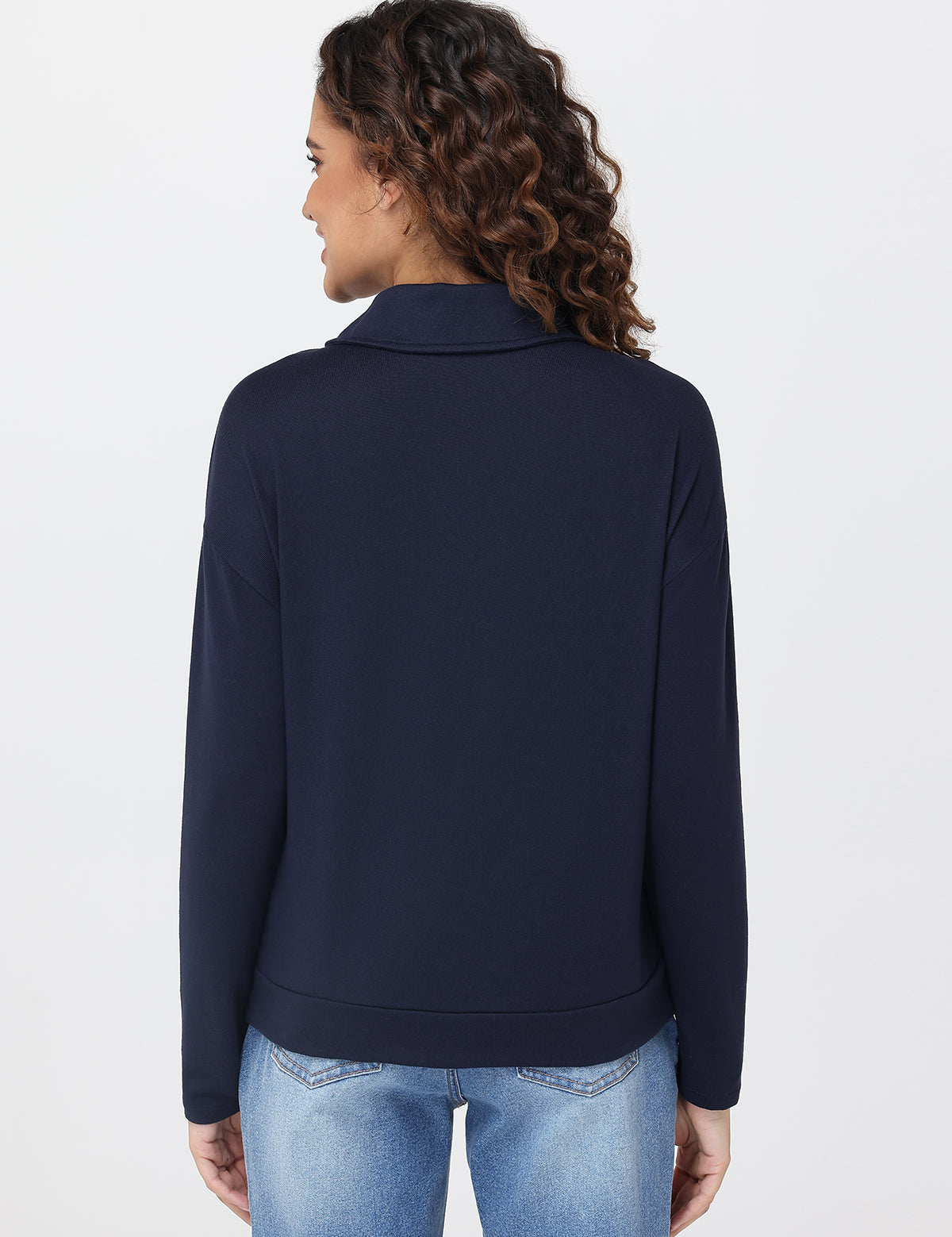 Person wearing a navy blue pullover and light blue jeans on a white background