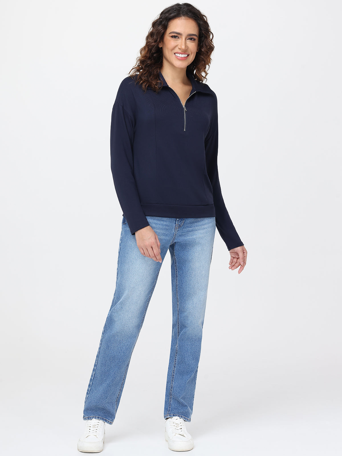 Woman wearing a navy long-sleeve top and light blue jeans on a white background