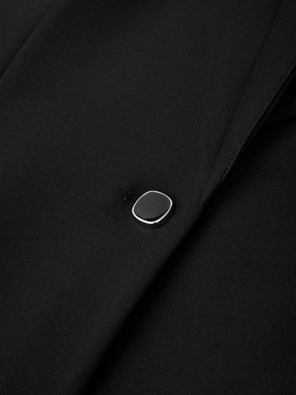 Close-up of a black fabric with a silver button on a dark background