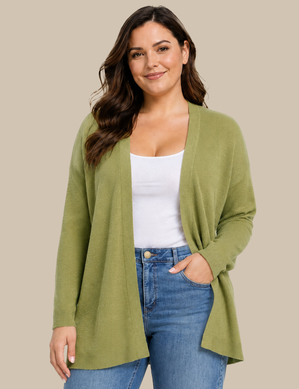 A woman modeling a sage green open-front cardigan over a white tank top and blue jeans, set against a solid beige studio background.
