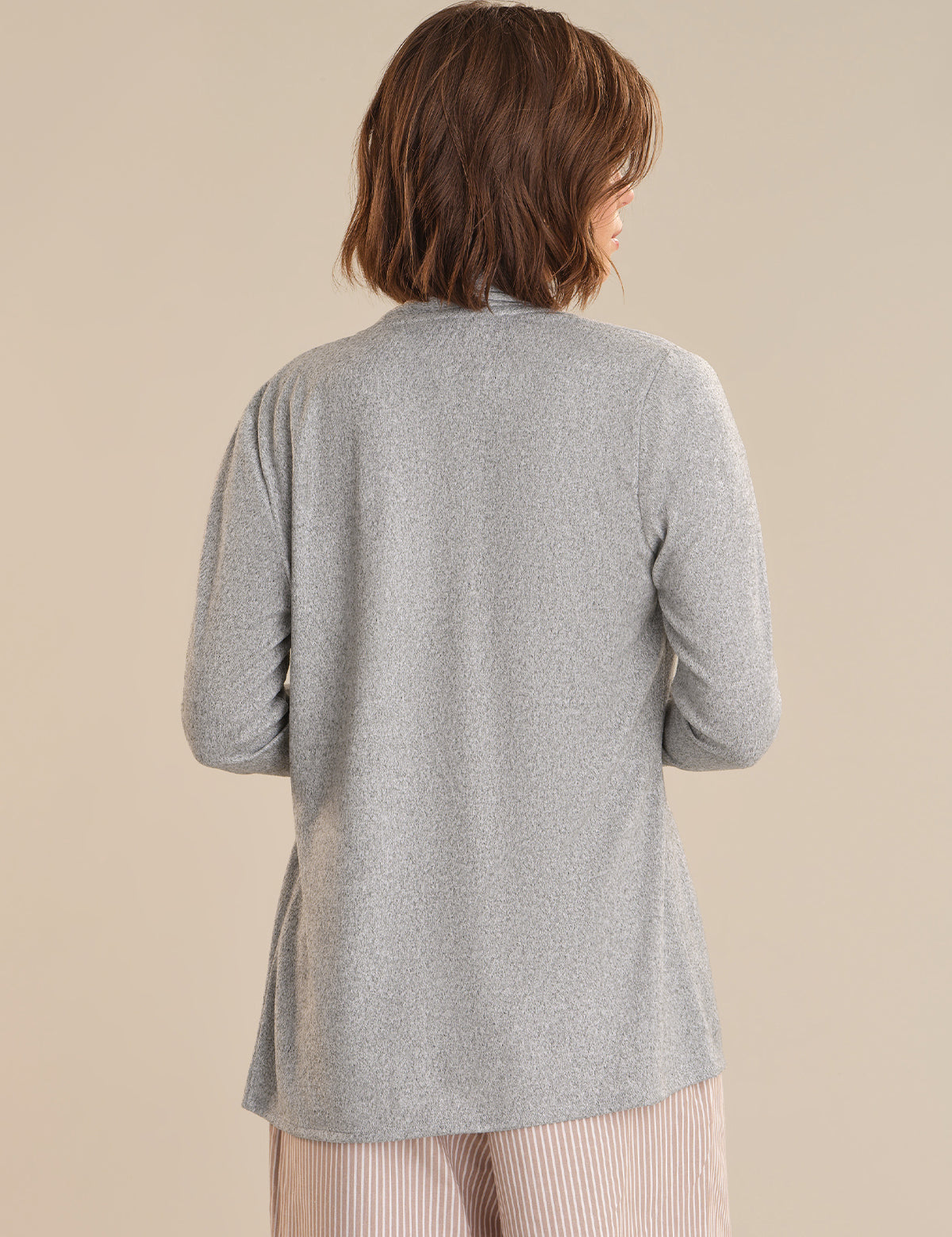 Person wearing a gray cardigan against a beige background