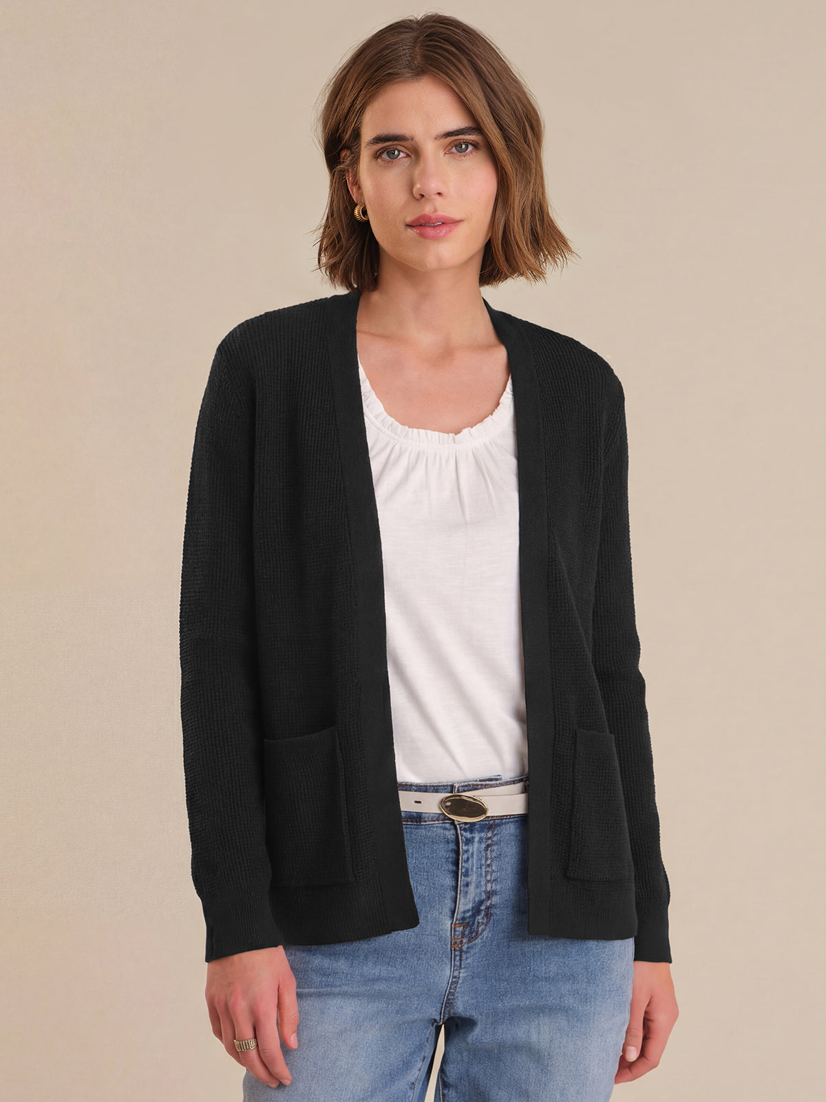 Woman wearing a black cardigan over a white shirt and blue jeans on a beige background