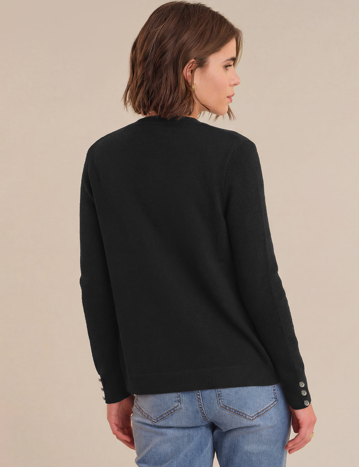 Woman wearing a black sweater and blue jeans against a beige background