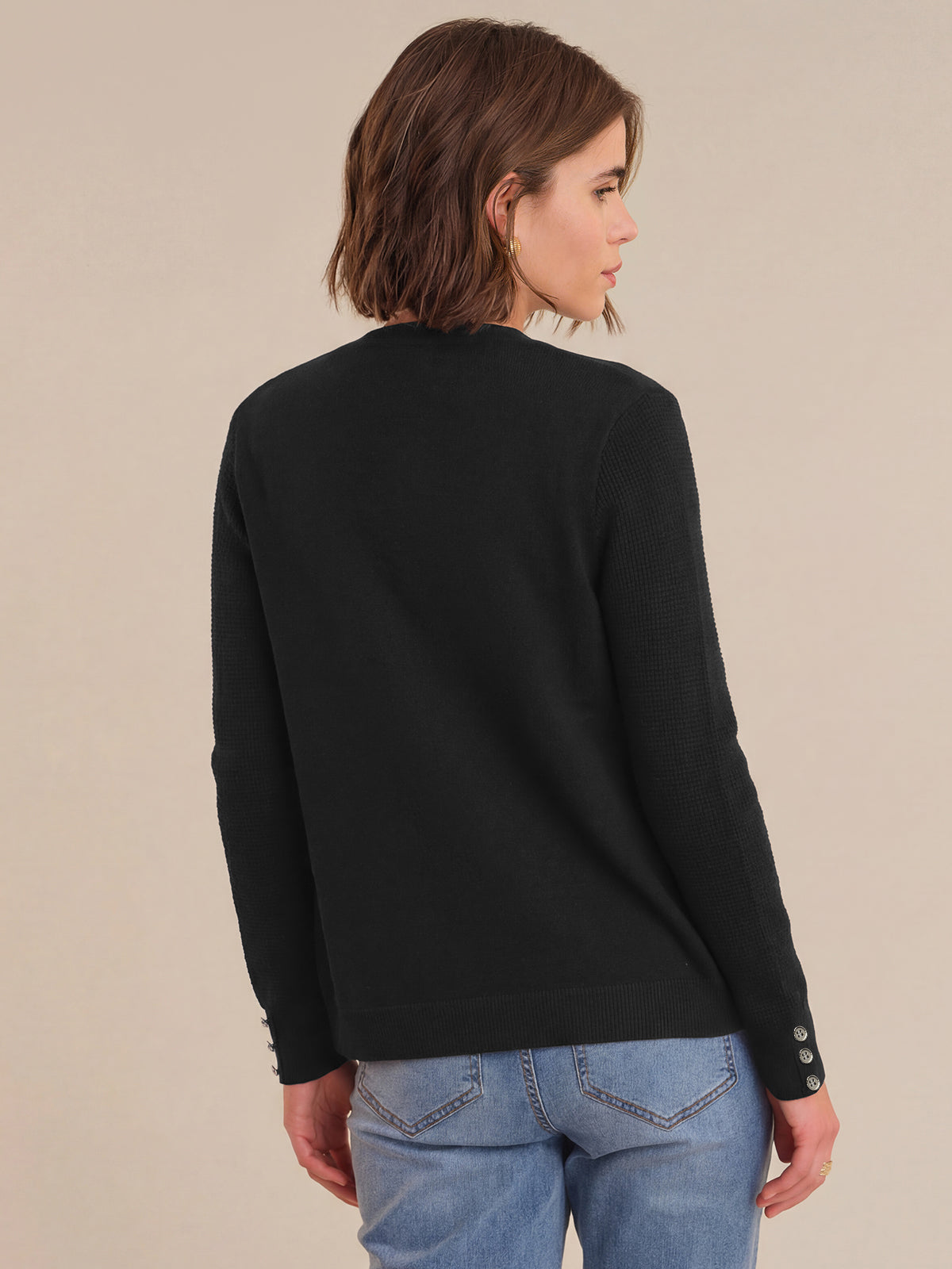Woman wearing a black sweater and blue jeans against a beige background