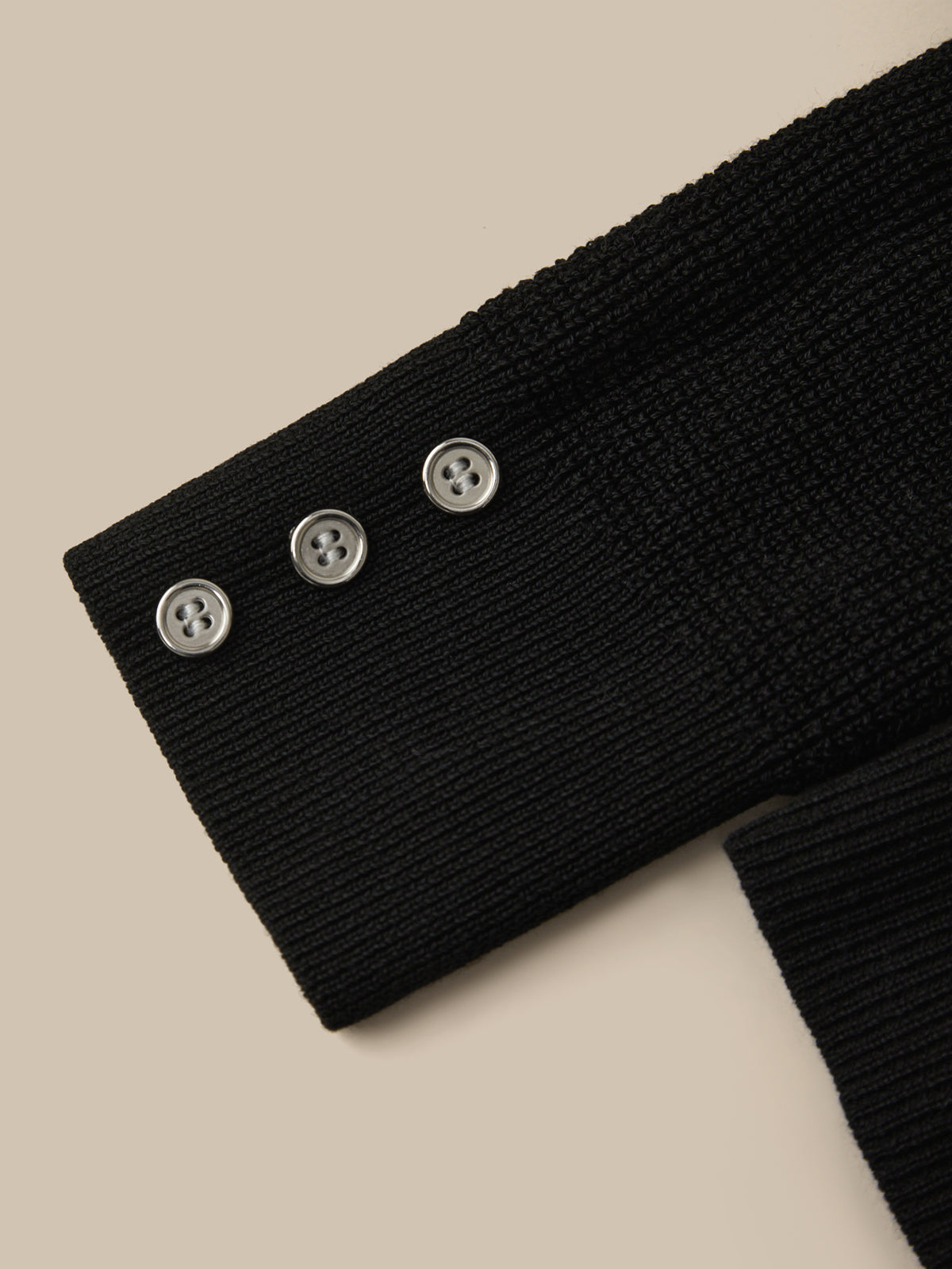 Close-up of a black ribbed sweater with button details on a beige background