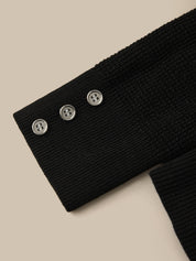 Close-up of a black ribbed sweater with button details on a beige background