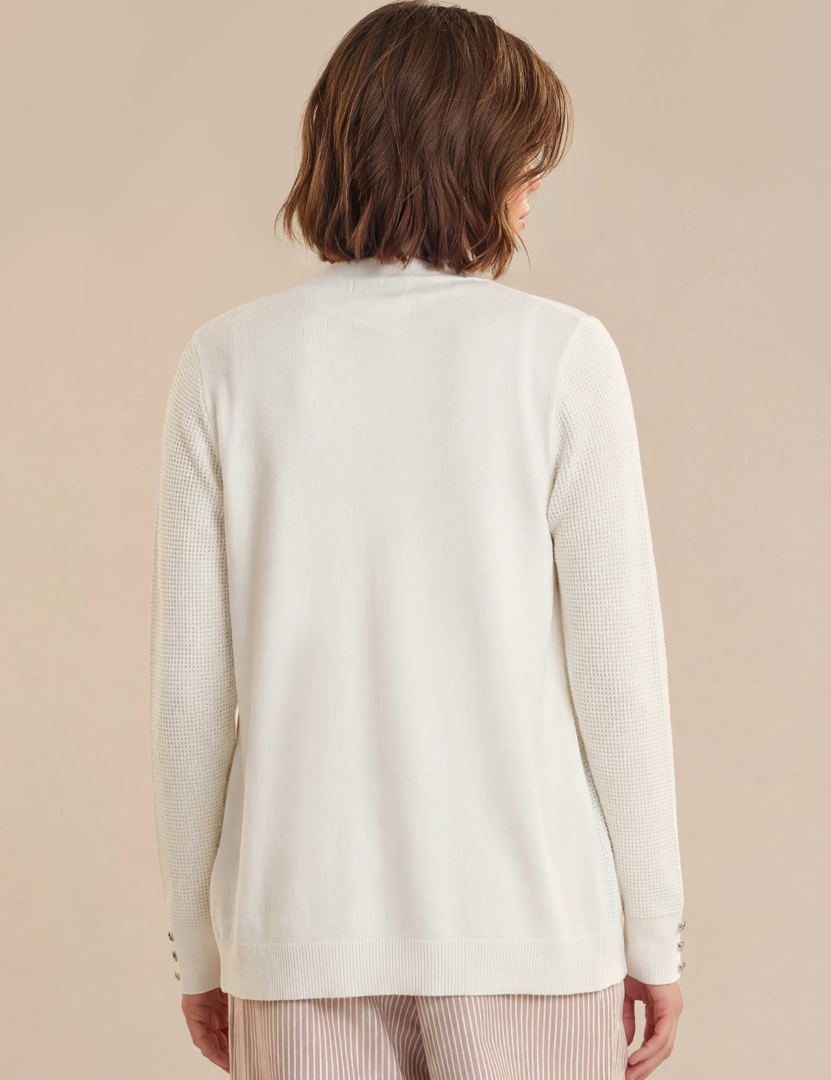 Person wearing a light-colored cardigan against a beige background