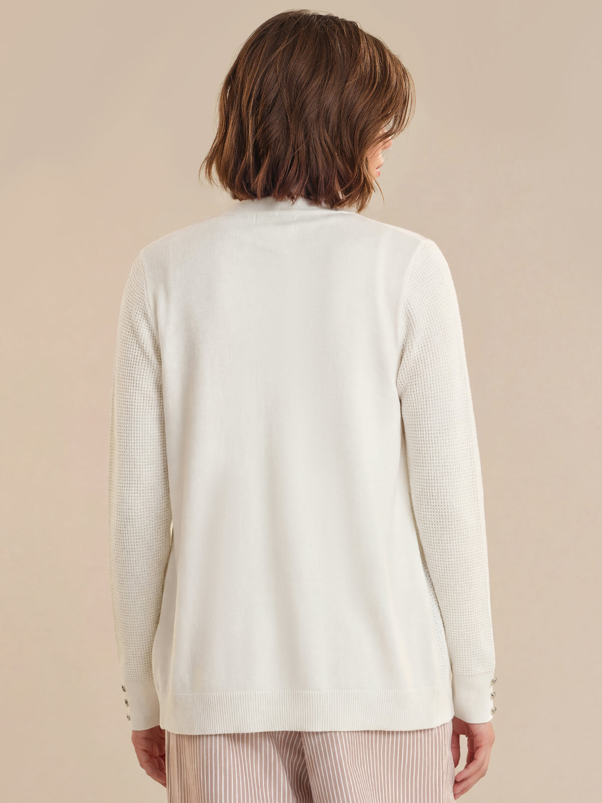 Person wearing a light-colored cardigan against a beige background