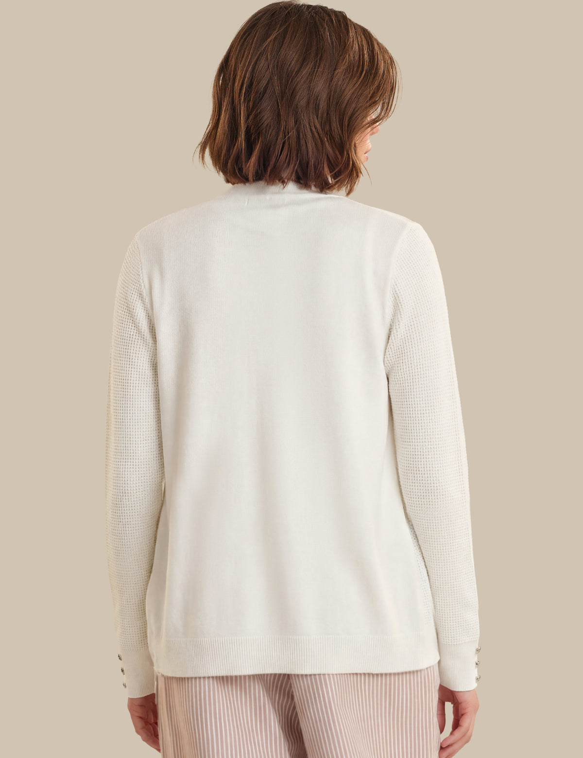 Person wearing a cream-colored cardigan on a beige background