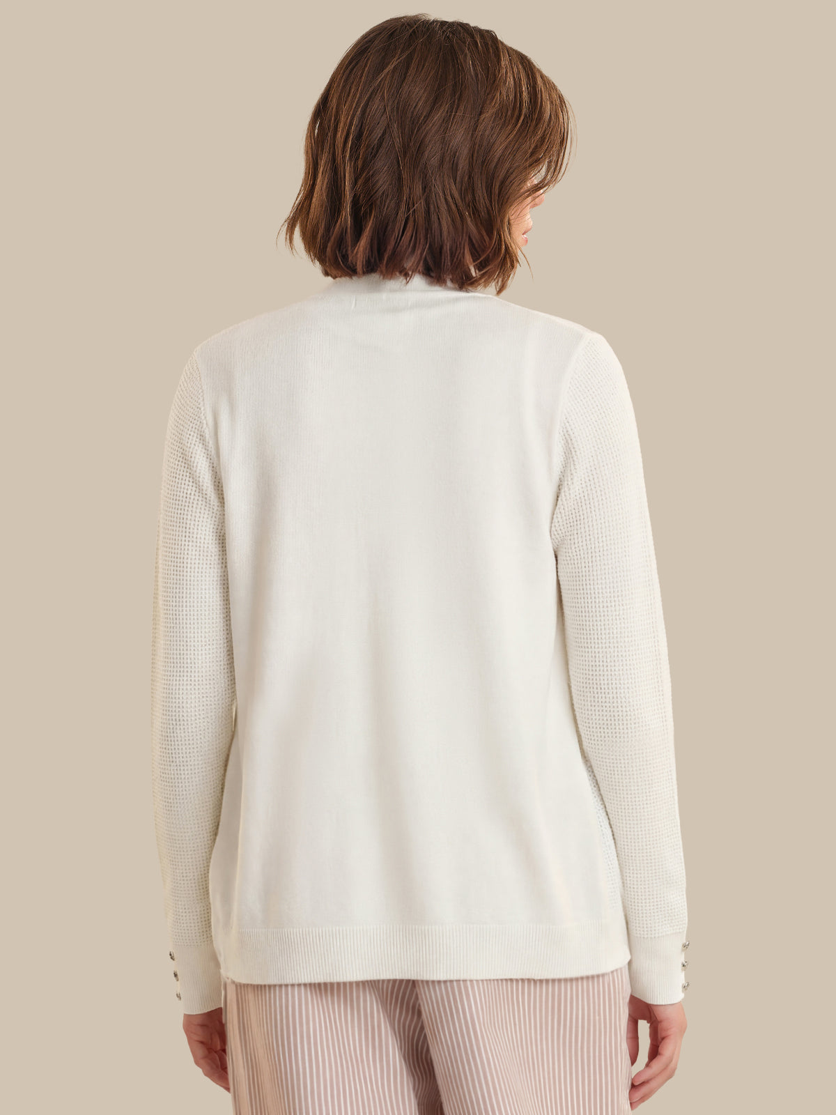 Person wearing a cream-colored cardigan on a beige background