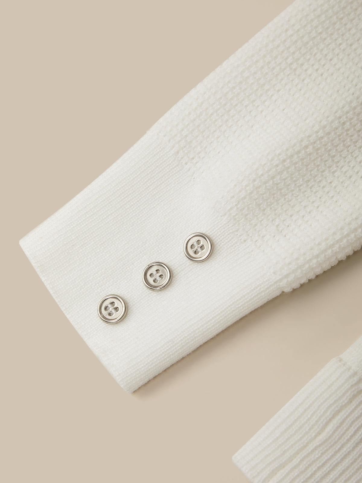 Close-up of a white textured fabric with three buttons on a beige background
