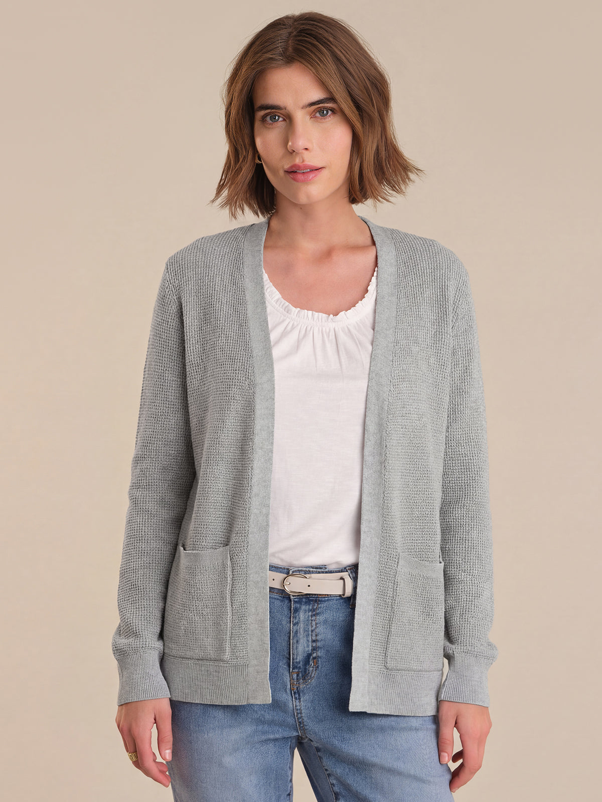 Woman wearing a gray cardigan over a white shirt and blue jeans on a beige background