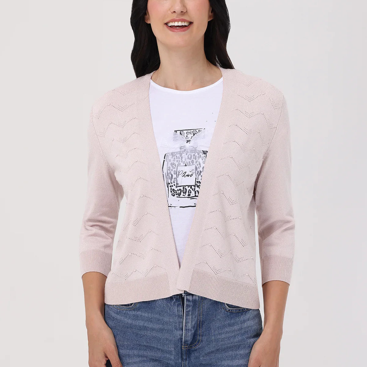 Woman wearing a light pink cardigan over a white shirt with a graphic design, standing against a plain background.