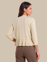 A woman shown from the back wearing a light beige cropped cardigan with three-quarter sleeves and a pleated hem, paired with brown pants, against a solid beige background.