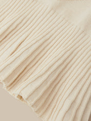 Close-up of a cream-colored ribbed knit fabric with a fringed edge, showing the detailed texture and weave.