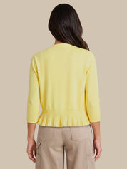 A woman viewed from the back wearing a pale yellow knit cardigan with three-quarter sleeves and a gathered pleated hem, paired with beige cargo pants, against a solid beige background.
