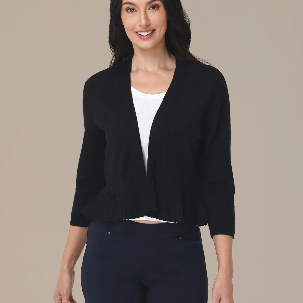 Woman wearing a black cardigan over a white shirt and dark pants on a beige background