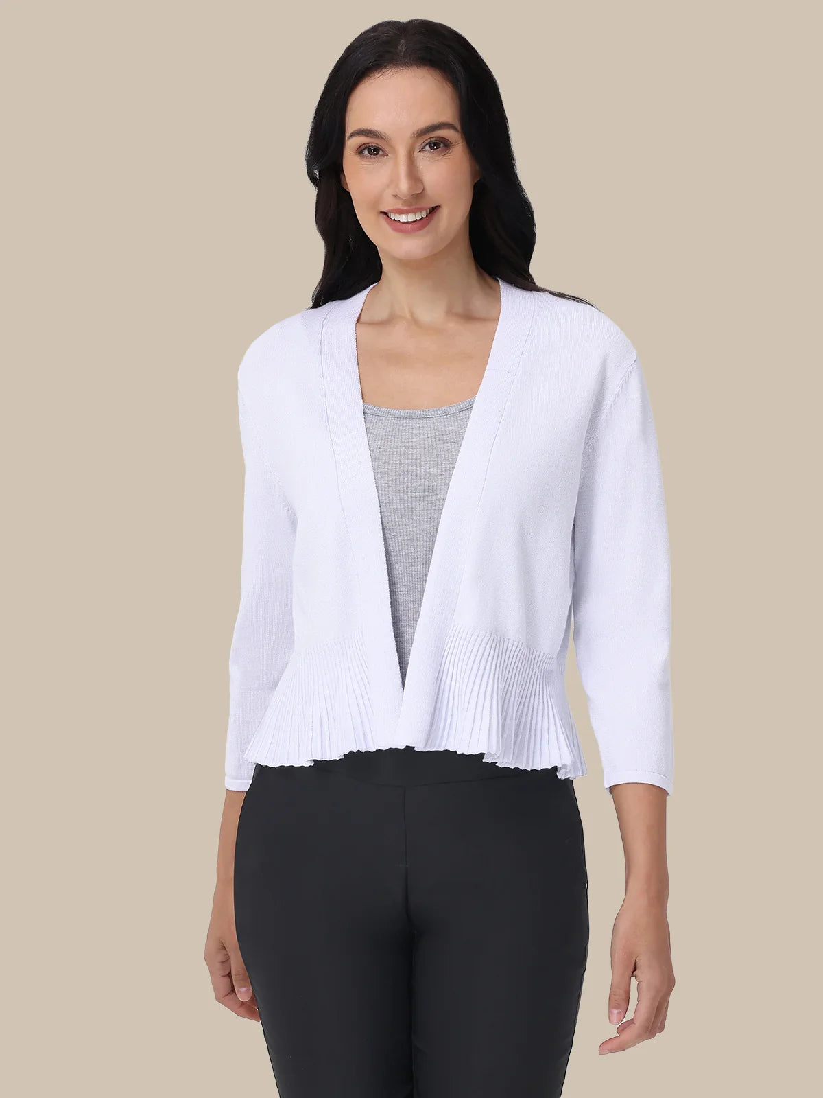 Woman wearing a white cardigan over a gray top and black pants on a beige background