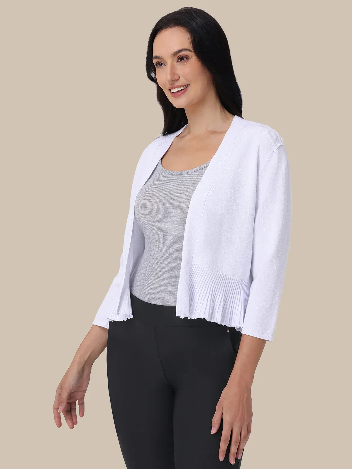 Woman wearing a white cardigan over a gray top and black pants on a beige background