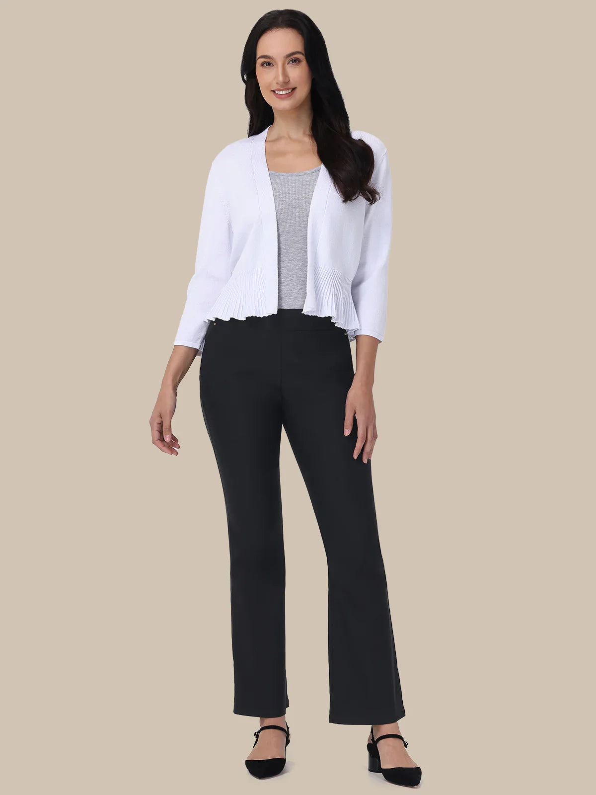 Woman wearing a white cardigan over a gray top and black pants on a beige background