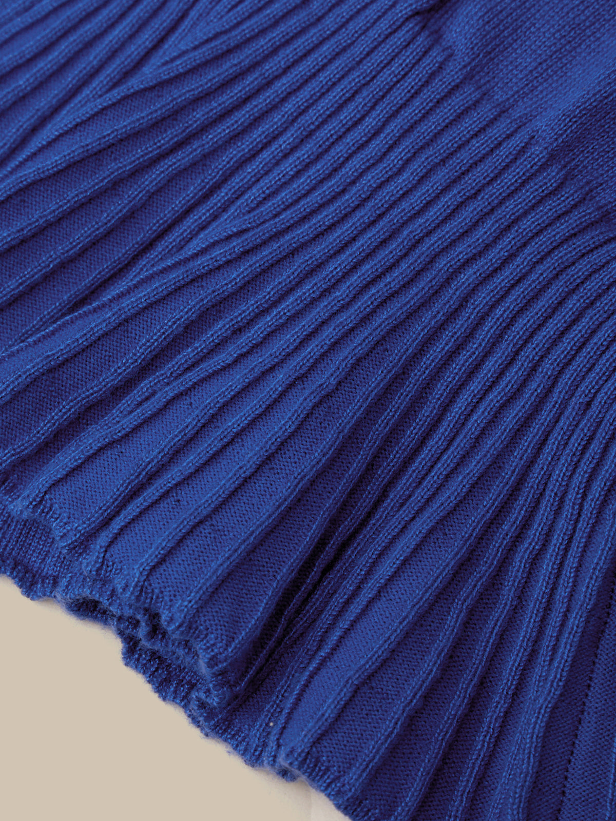 A close-up of a royal blue ribbed knit fabric, showing the detailed vertical pleats and texture, with a small portion of a light beige surface visible at the bottom left.