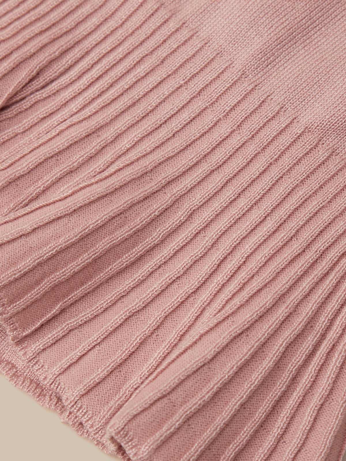 Close-up of a dusty pink ribbed knit fabric texture, showing the detailed vertical corduroy-like weave and fringed edge.