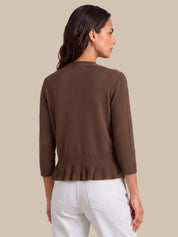 A woman shown from the back wearing a brown knit cardigan with three-quarter sleeves and a pleated hem, paired with white pants, against a solid beige background.