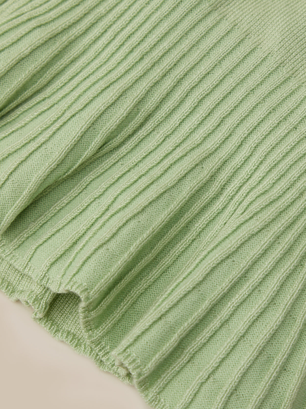 Close-up of a light sage green ribbed knit fabric with a frayed hem, showing the detailed texture and weave.