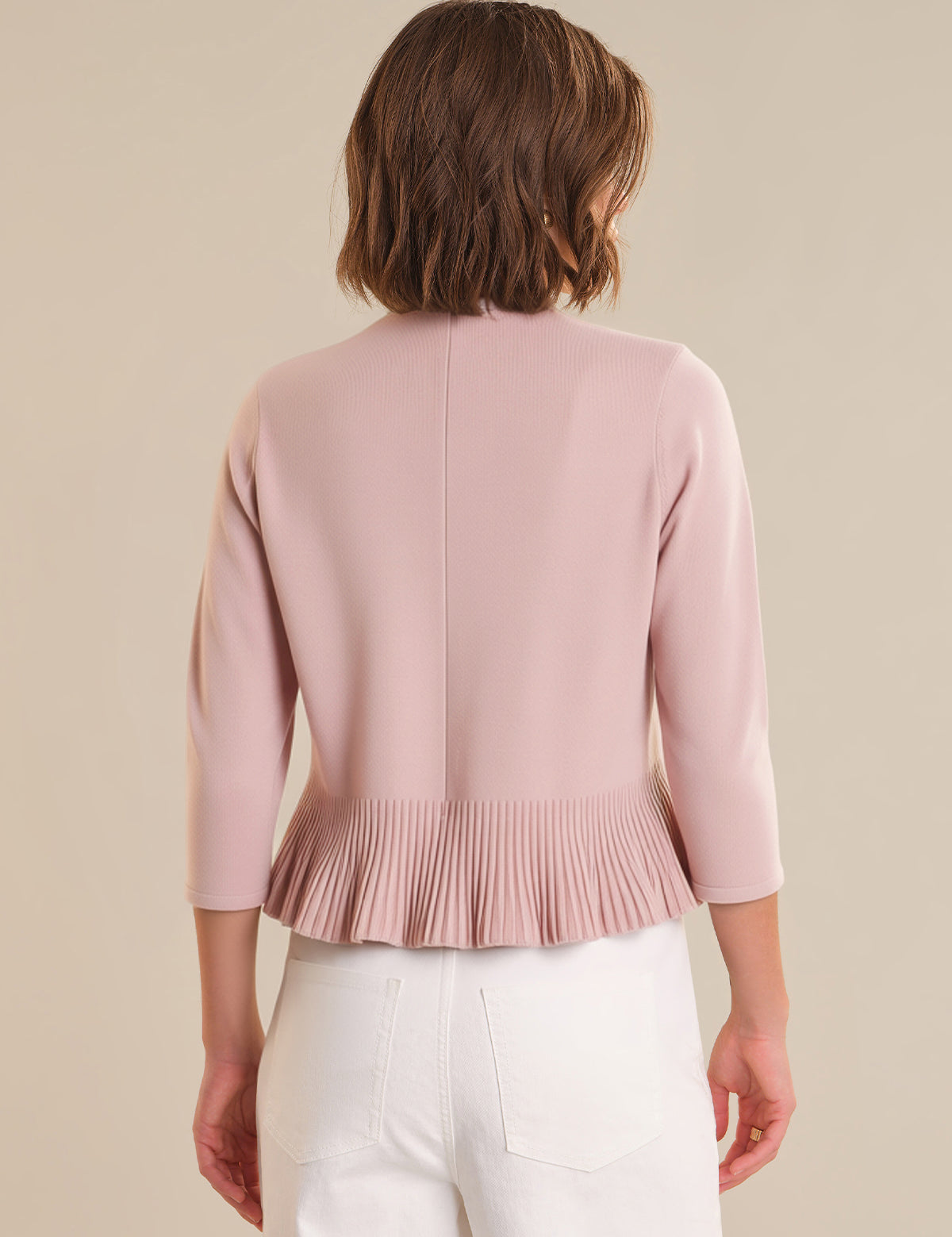 Woman wearing a light pink peplum top against a beige background