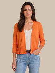 A woman modeling a bright orange open-front cardigan with three-quarter sleeves and a pleated hem, worn over a cream ribbed top and blue jeans against a solid beige background.