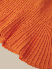 Close-up of a bright orange ribbed knit fabric with a frayed hem, shown against a light beige background.