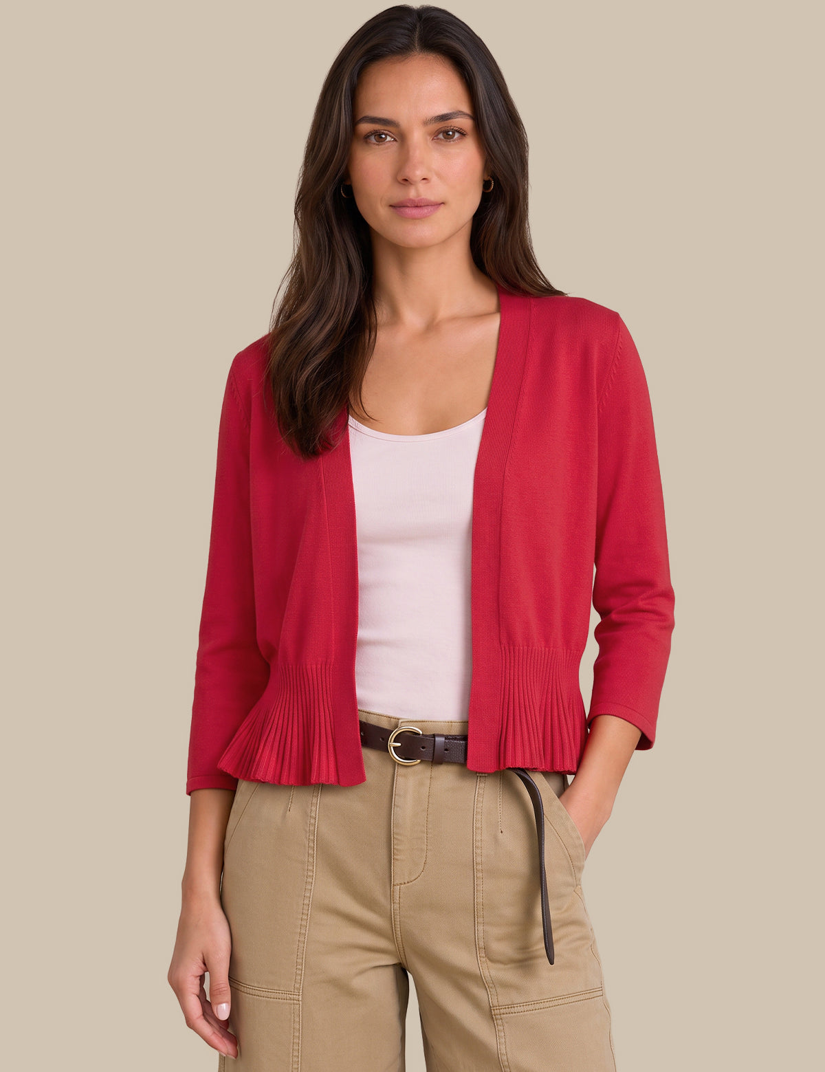 A woman modeling a bright red open-front cardigan with pleated ruffle trim at the hem and cuffs, worn over a light pink top and khaki pants against a solid beige background.