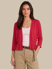 A woman modeling a bright red open-front cardigan with pleated ruffle trim at the hem and cuffs, worn over a light pink top and khaki pants against a solid beige background.