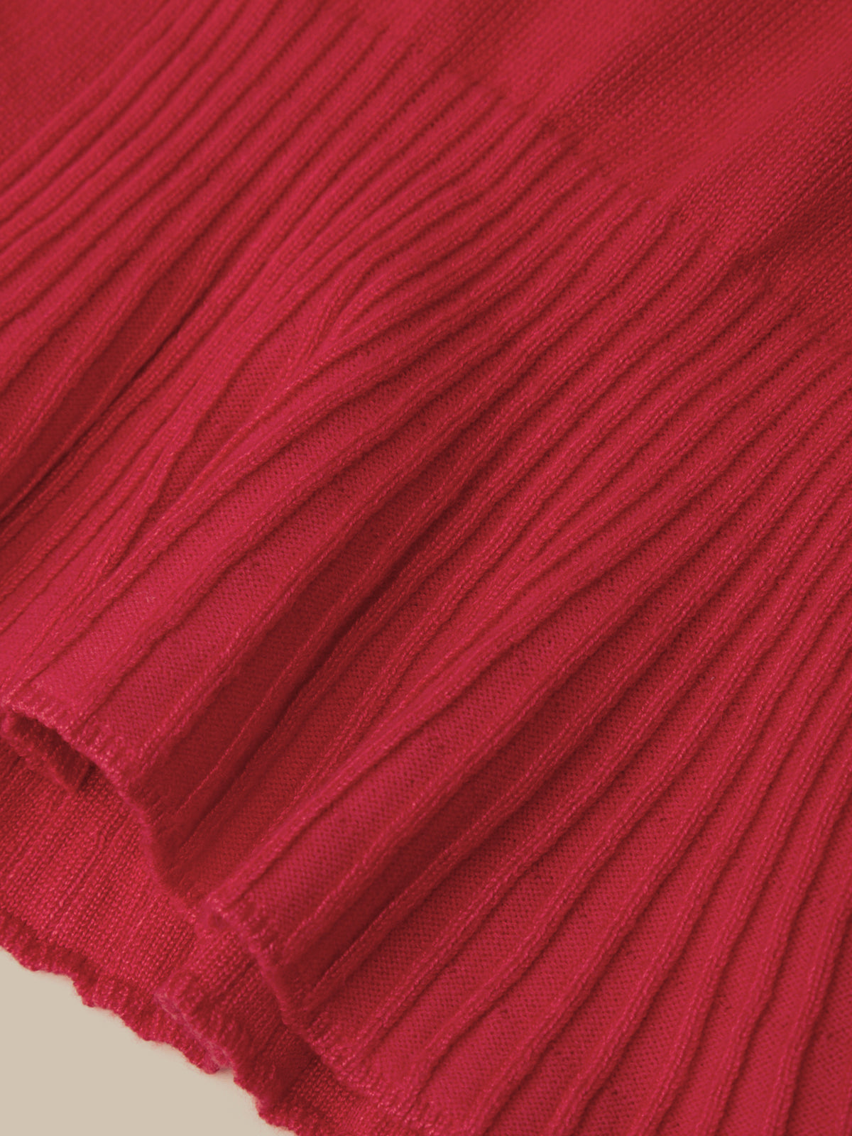 A close-up of a vibrant red ribbed knit fabric, showing the detailed vertical pleats and texture of the material.