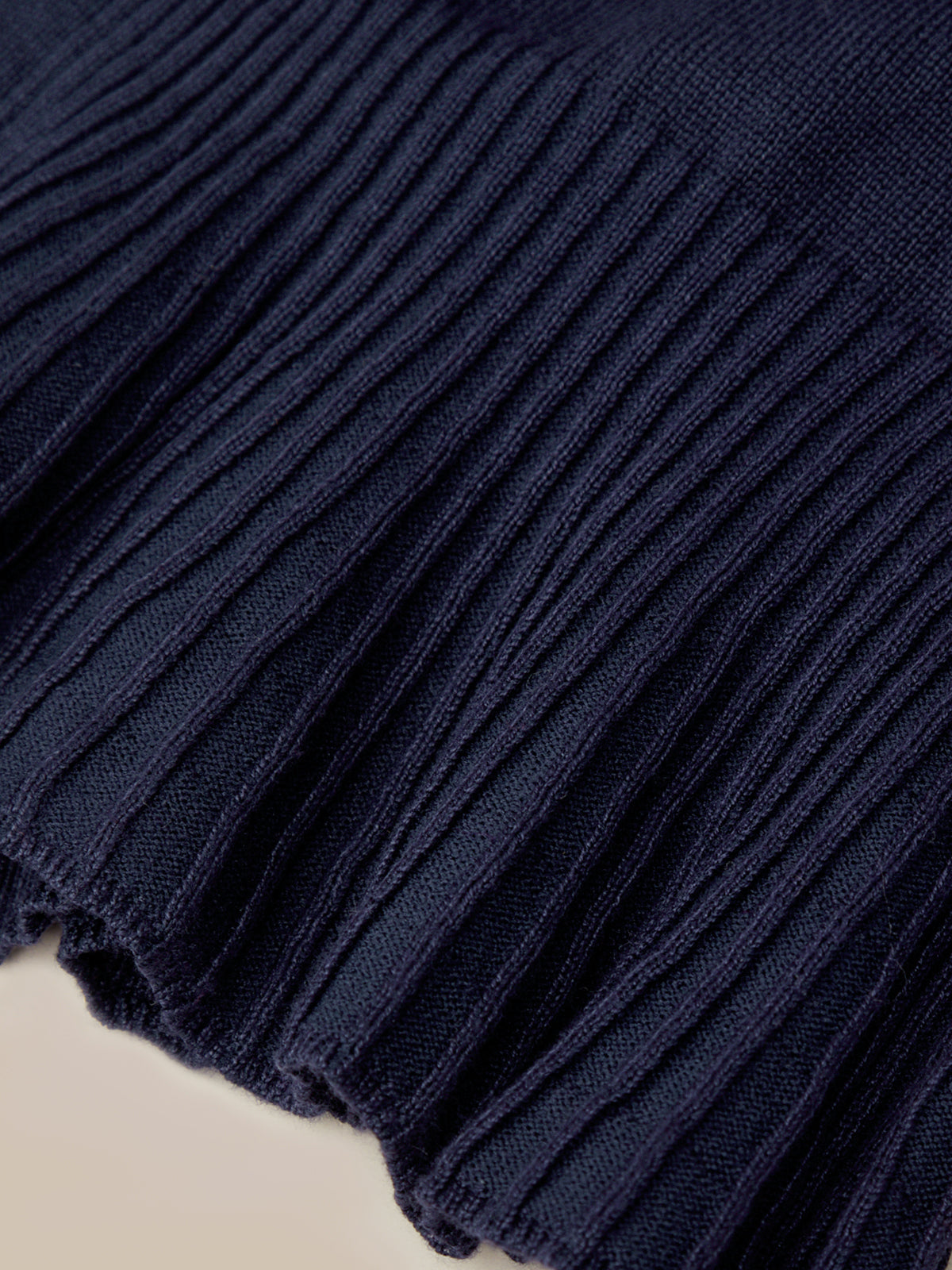 Close-up of a dark navy blue ribbed knit fabric, showing the detailed vertical corduroy-like texture and frayed edge.