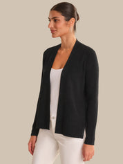 Woman wearing a black cardigan over a white shirt and pants on a beige background