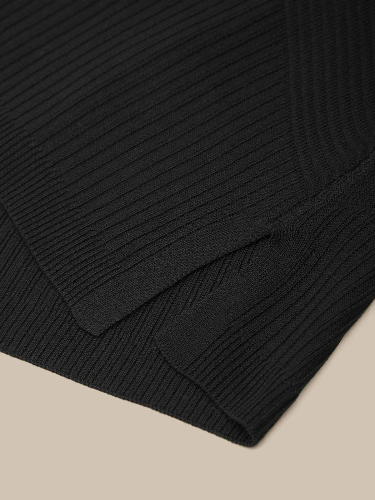 Close-up of a black ribbed sweater on a beige background