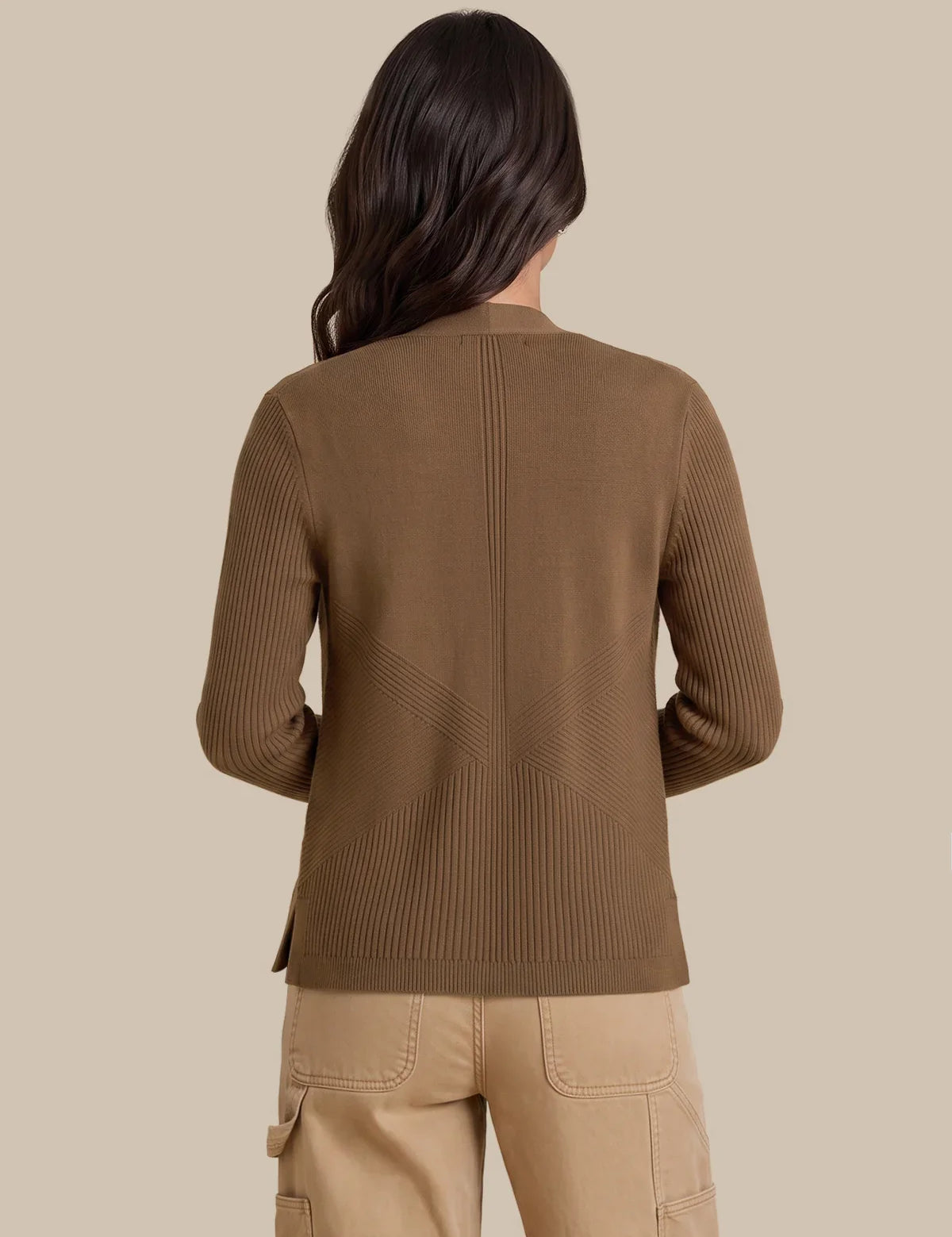 A woman shown from the back wearing a brown ribbed knit sweater and beige cargo pants against a solid beige studio background.