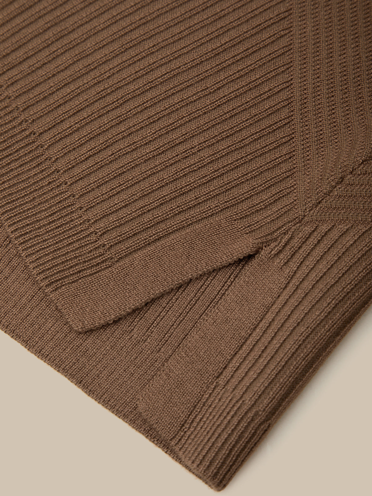 Close-up of a brown ribbed knit fabric, showing the texture and folded corner of the garment on a light beige background.