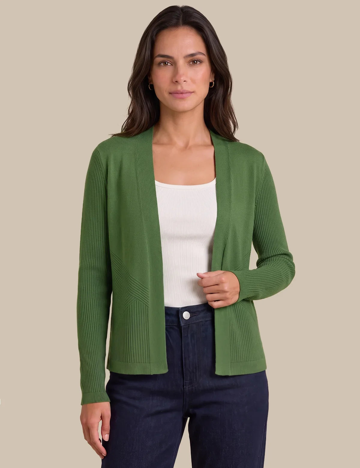 A woman modeling a green ribbed knit cardigan over a white tank top and dark blue jeans, set against a solid beige background.