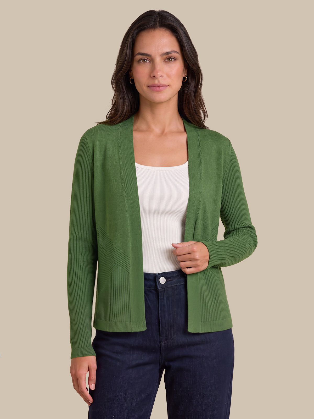 A woman modeling a green ribbed knit cardigan over a white tank top and dark blue jeans, set against a solid beige background.