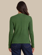 A woman viewed from the back wearing a green ribbed knit sweater and dark blue jeans against a solid beige background.