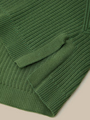Close-up of a dark green ribbed knit fabric, showing the texture and folded edges of a garment on a light beige background.