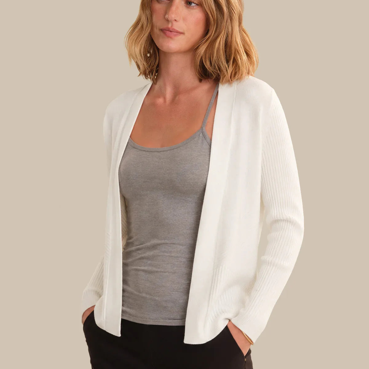 Woman wearing a white cardigan over a gray top with a beige background
