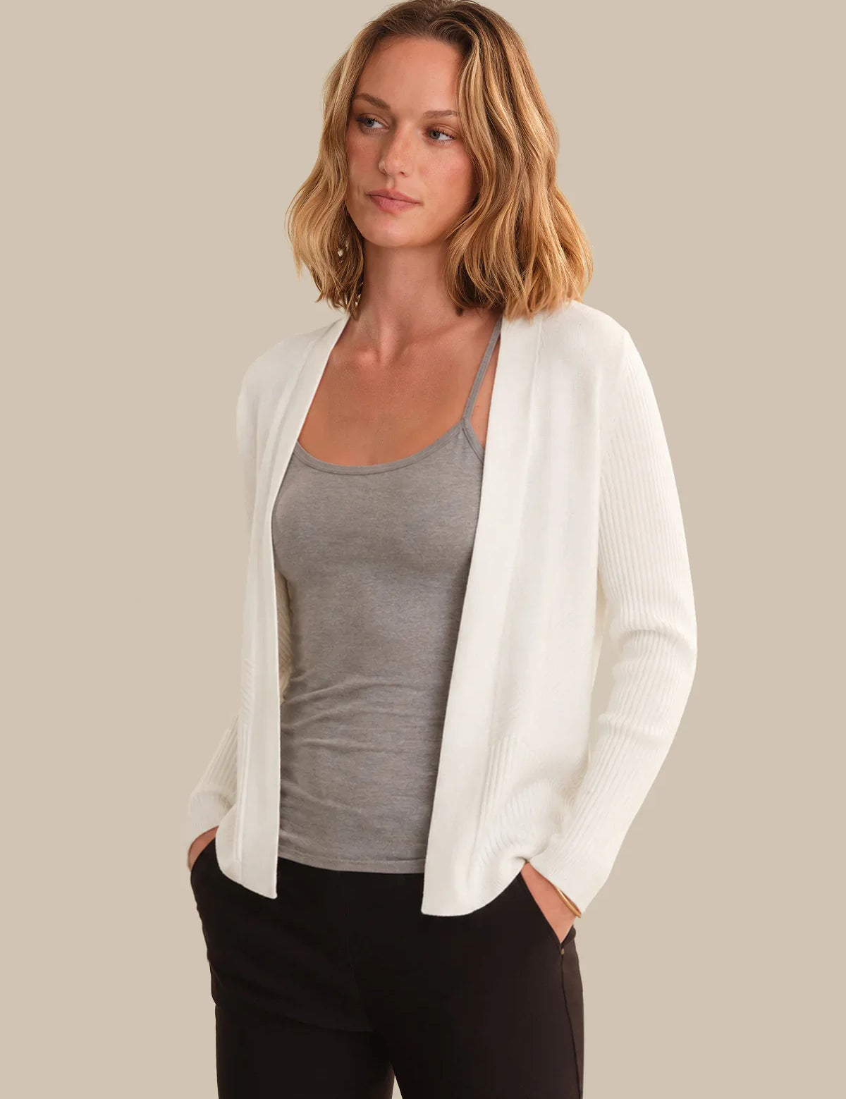Woman wearing a white cardigan over a gray top with a beige background