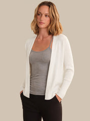 Woman wearing a white cardigan over a gray top with a beige background
