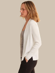 Woman wearing a white cardigan over a gray top and black pants on a beige background