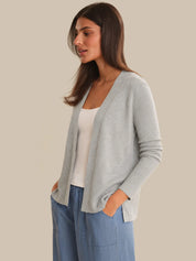 Woman wearing a light gray cardigan over a white top and blue jeans on a beige background